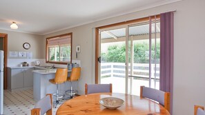 Eine kompakte Küche mit Spüle, einer Uhr und einem Telefon. Ein Essbereich mit Tisch und Stühlen, und eine Schiebeglastür, die auf einen Balkon führt.