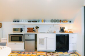 A compact kitchen with a microwave, refrigerator, dishwasher, and a shelf with various glassware.