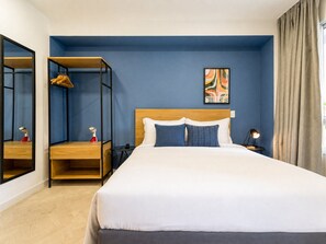 Habitació d'hotel ben ordenada amb llit, taulella de nit, taula auxiliar, mirall i armari.
