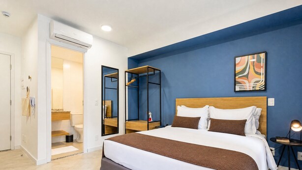 A hotel room with a bed, a bedside table, a mirror, a bathroom with a toilet, and a shower. - Mobi Pinheiros (São Paulo)
