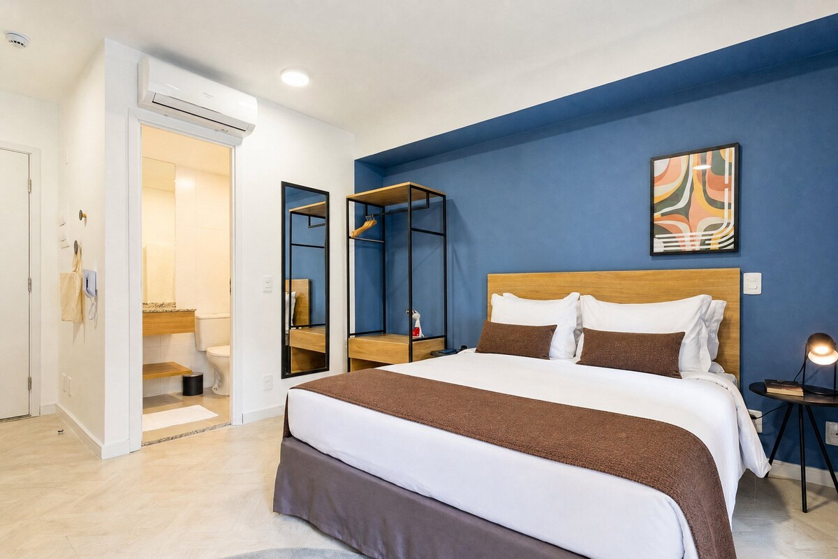 A hotel room with a bed, a bedside table, a mirror, a bathroom with a toilet, and a shower.