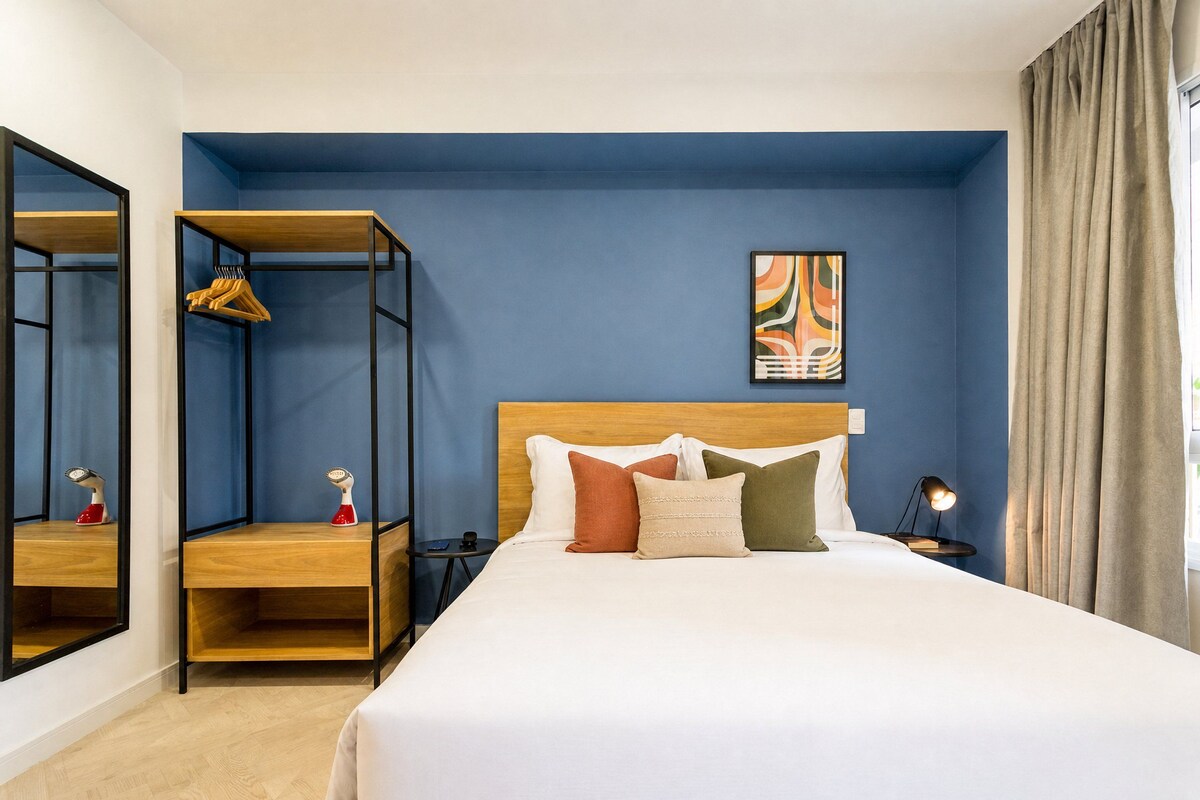 A hotel room with a bed, a nightstand, a bedside table, a mirror, a wardrobe, and a painting on the wall.