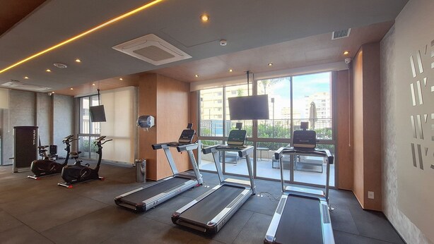 A gym with treadmills, stationary bikes, and a television screen. - Nex One Paraiso (São Paulo)