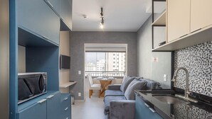 A compact kitchen with a dining area, a sofa, and a view of the city through a window. - Nex One Paraiso (São Paulo)