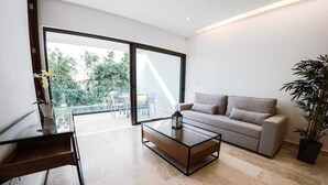 A modern living room with a glass coffee table, a sofa, and a large sliding glass door leading to an outdoor area. - Beautiful One-Bedroom, Two-Full-Bathroom Condo Just Steps from the Beach! (Playa del Carmen)