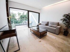 Ein modernes Wohnzimmer mit einem Glastisch, einer Couch und einer großen Schiebeglastür, die zu einem Außenbereich führt.