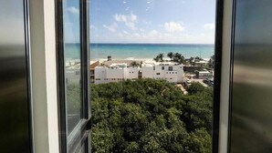 A view through a window of a coastal area with buildings, trees, and the ocean. - Beautiful One-Bedroom, Two-Full-Bathroom Condo Just Steps from the Beach! (Playa del Carmen)