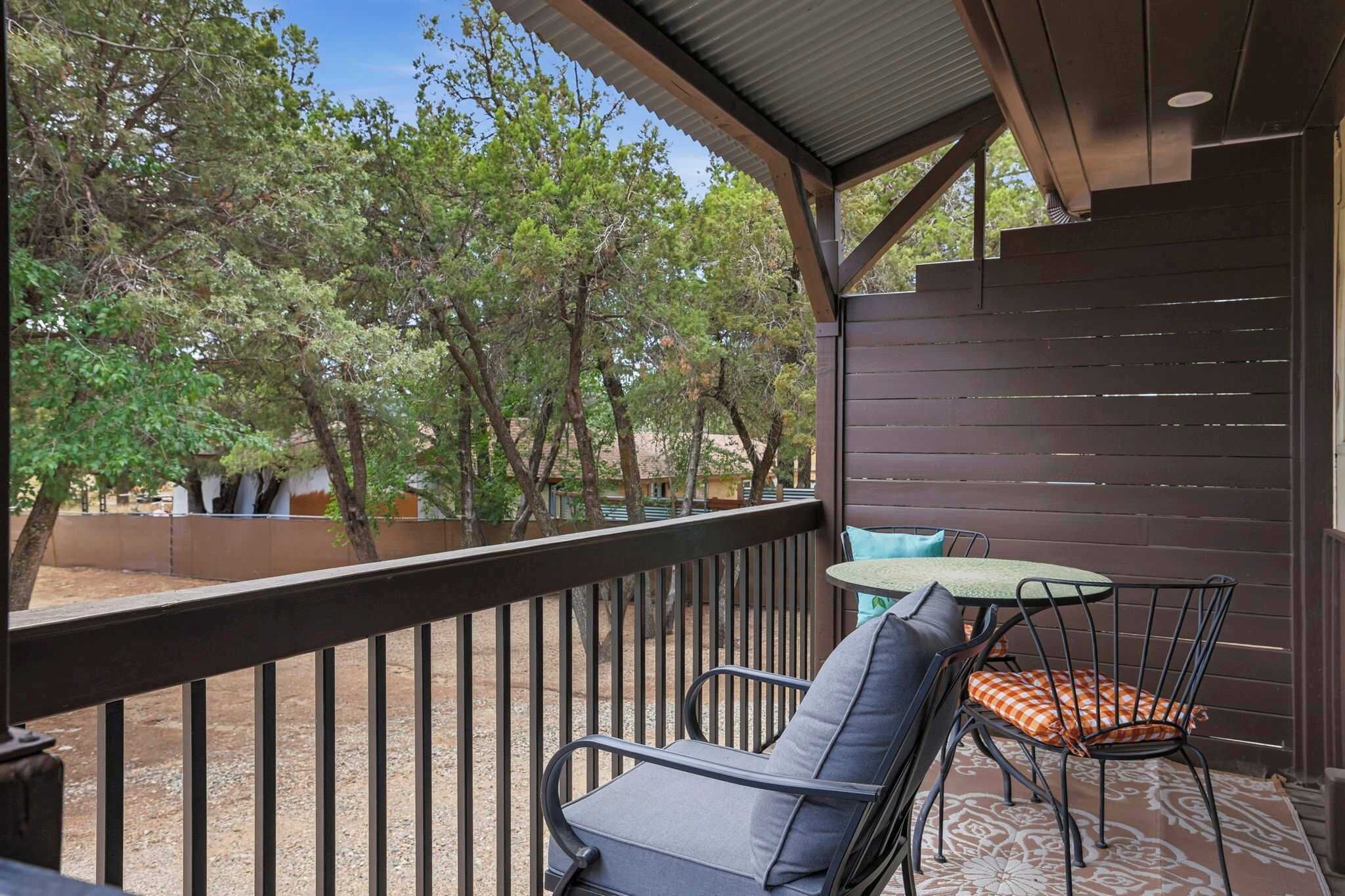 A balcony with a table and chairs, surrounded by a railing, overlooking a wooded area.