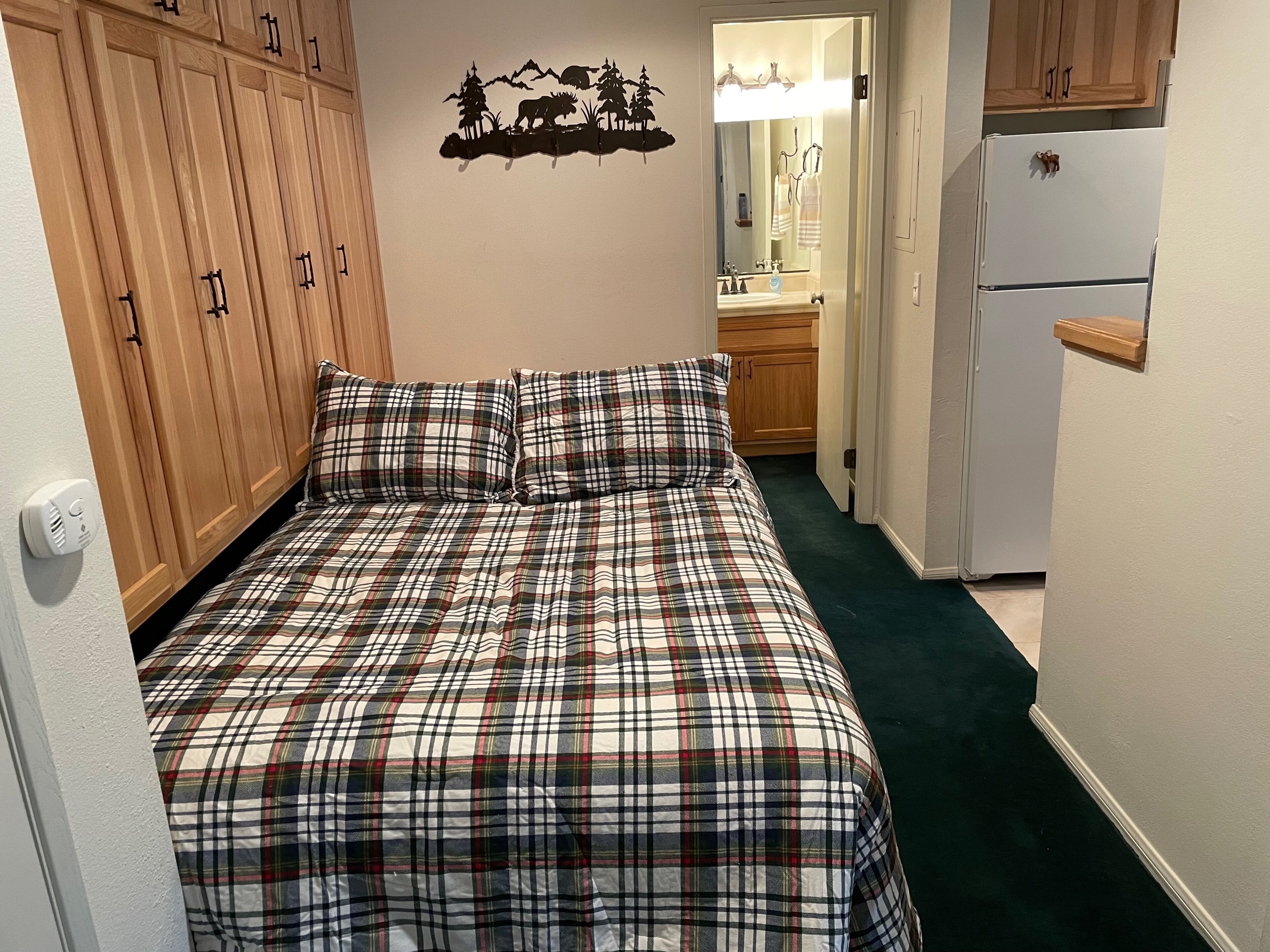 Une chambre avec une couvre-lit à carreaux, une armoire en bois et un miroir au-dessus du lavabo.