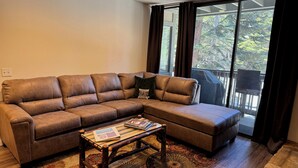Ein braunes, ledernes Ecksofa mit passendem Hocker, ein Couchtisch aus Holz mit einer Zeitschrift und ein gemustertes Teppich.