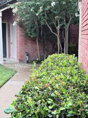 A brick building with a door, a small garden area with green shrubs, and trees in the background. - Cozy 1-bedroom condo in charming Houston with AC (Houston)
