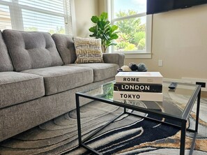 A living room with a grey sofa, a glass coffee table, and a plant. - Family-Friendly Houston Home - Near NRG, Med Center & Downtown (Houston)