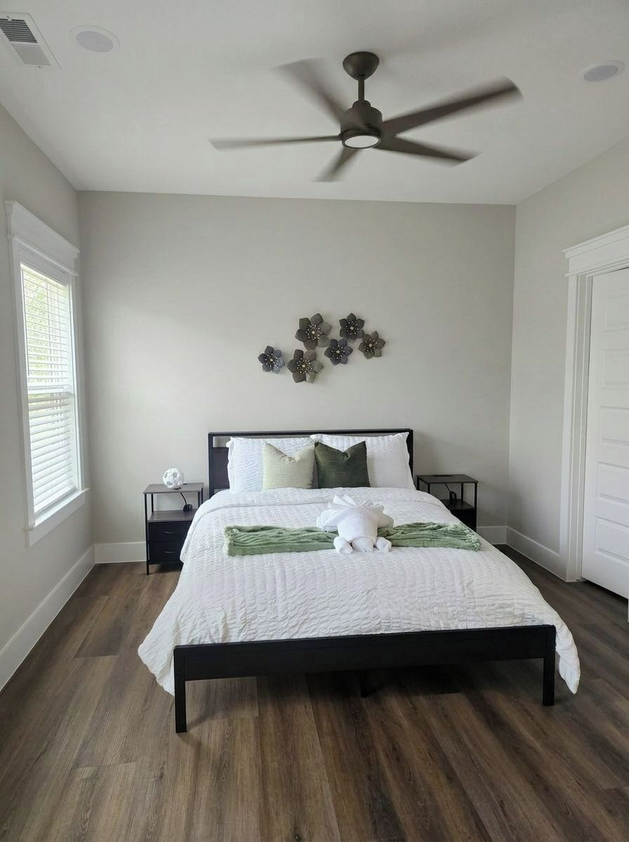 A bedroom with a bed, a ceiling fan, a nightstand, a wall decoration, and a window.