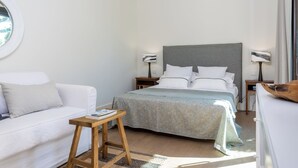 Ein Schlafzimmer mit einem Bett, einem Nachttisch, einer Lampe, einem kleinen Holzschemel und einem Fenster.
