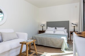 Ein Schlafzimmer mit einem Bett, einem Nachttisch, einer Lampe, einem kleinen Holzschemel und einem Fenster.