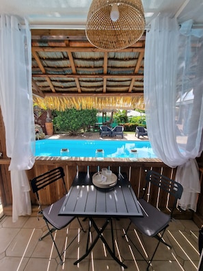 Eine Terrasse mit Holztisch und -stühlen, einer hängenden Leuchte und Blick auf einen Swimmingpool.