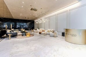 A hotel lobby with a marble floor, elegant sofas, a reception desk, and a chandelier. - Villa Versace (São Paulo)