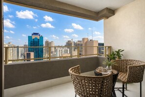 A balcony with wicker furniture, a table, and a view of a cityscape with high-rise buildings. - Villa Versace (São Paulo)