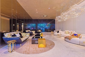 A luxurious living room with a modern chandelier, a large sofa set, and a unique wall art installation. - Villa Versace (São Paulo)