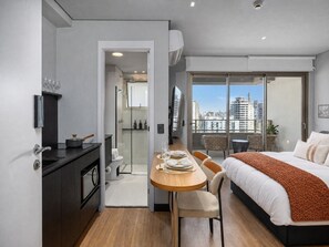 Een moderne hotelkamer met balkon, een eethoek, een douche en een bed.