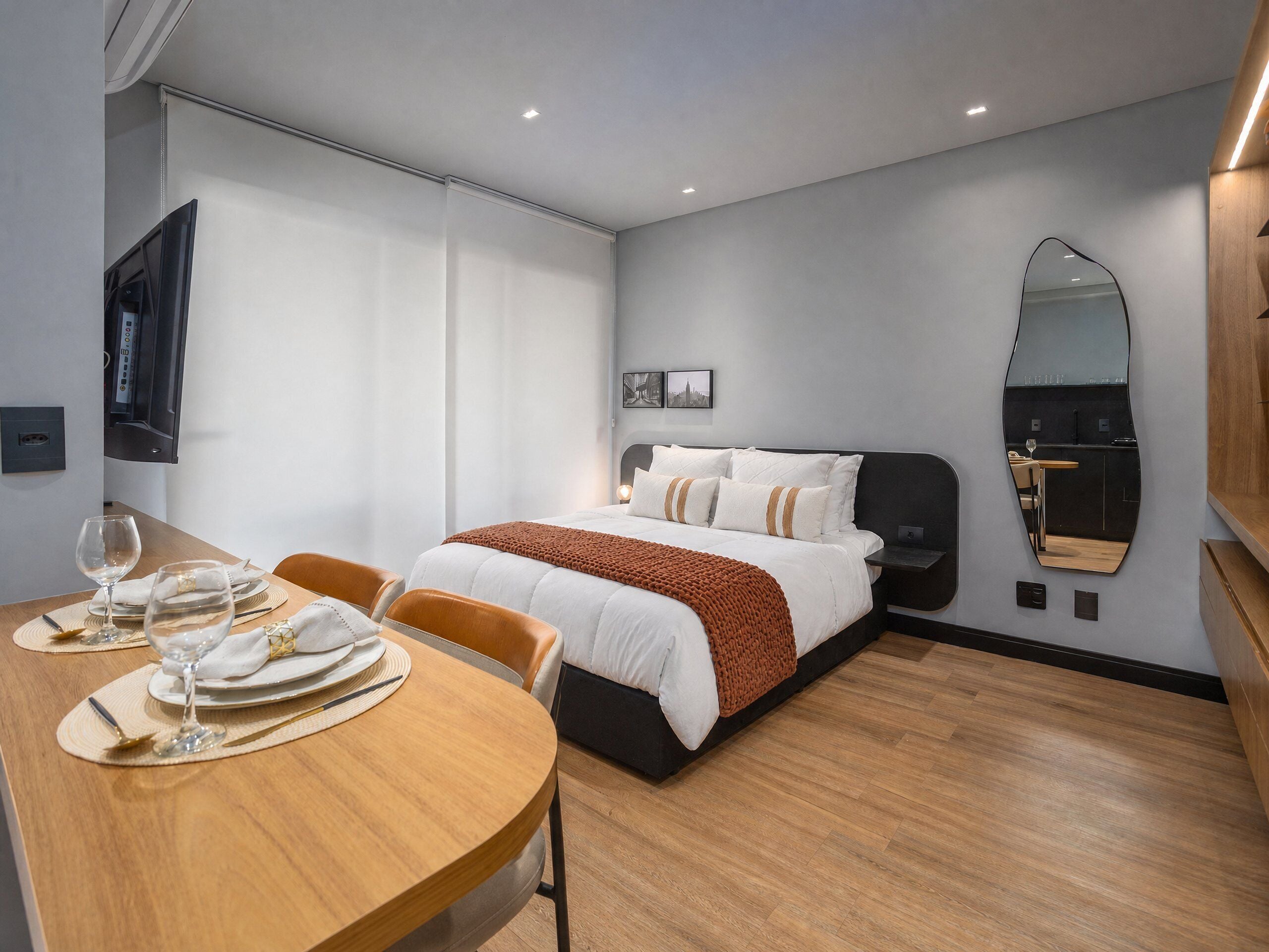 A hotel room with a bed, a dining table with chairs, a TV, and a mirror.