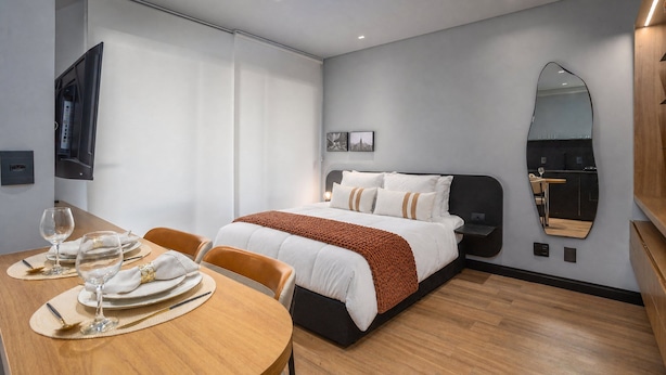 A hotel room with a bed, a dining table with chairs, a TV, and a mirror.
