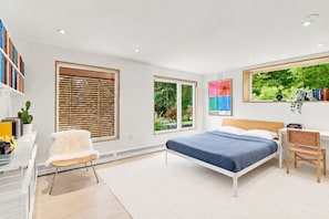 A modern bedroom with a bed, a desk, a chair, and large windows. - Charming 2BR Hanover Apt | Walk to Dartmouth (Hanover)