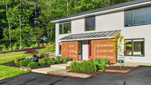 A modern two-story house with a landscaped garden, a driveway, and a large window on the second floor.