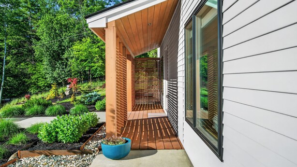 A modern house with a wooden deck, a large window, and a garden with various plants.