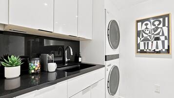 A modern kitchen with white cabinets, a black countertop, a sink, and a washing machine.