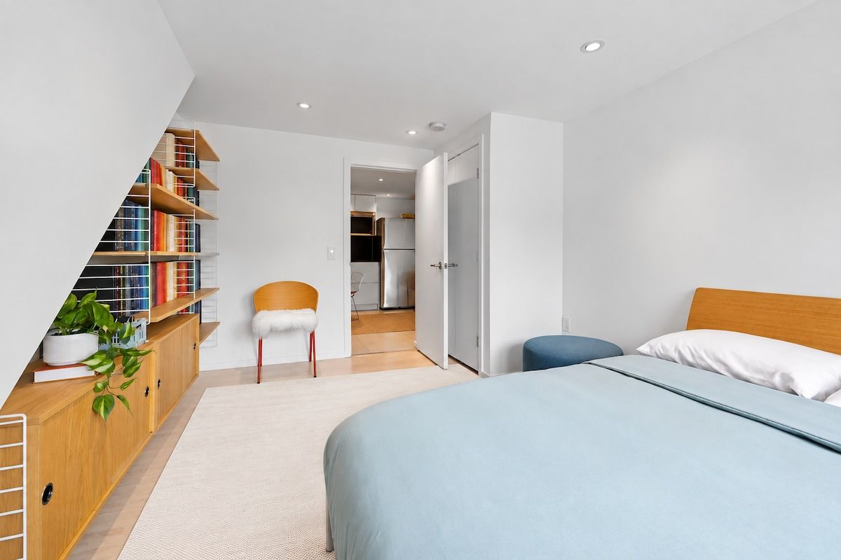 Une chambre avec un lit, une bibliothèque, une chaise et une vue sur la cuisine.