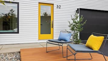 A modern house with a yellow door, numbered 32, and a deck with two lounge chairs and a small tree.