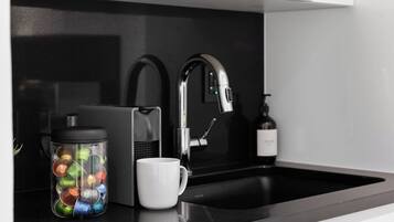 Une cuisine moderne avec un plan de travail noir, un robinet en acier inoxydable, une machine à café et une tasse.