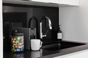 A modern kitchen with a black countertop, a stainless steel faucet, a coffee maker, and a mug.