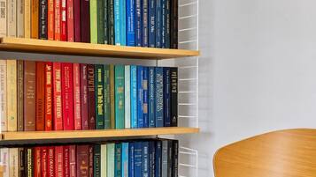 Une bibliothèque remplie de divers livres, une chaise aux pieds rouges et un coussin blanc et moelleux.