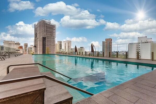 Une piscine sur le toit offrant une vue sur les bâtiments environnants, un ciel dégagé et une journée ensoleillée.
