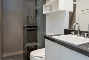 A modern bathroom with a glass shower enclosure, a white toilet, and a sink with a granite countertop. - VN Capote Valente (São Paulo)