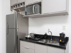 A compact kitchen with a built-in microwave, a sink, and a stove. - VN Capote Valente (São Paulo)