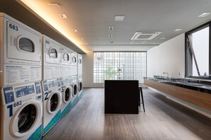 A modern laundry facility with multiple washing machines, a large window, and a counter with sinks. - VN Capote Valente (São Paulo)