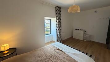 Un dormitorio con cama, mesita de noche con lámpara, armario, lámpara colgante y ventana con vistas al exterior.