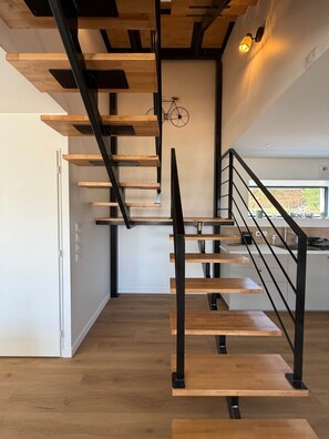 Eine moderne Treppe mit Holzbodenstufen und schwarzen Metallgeländern, die zu einem Küchenbereich mit einem Fenster führt.