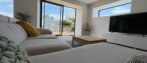 A modern living room with a sofa, a coffee table, a flat-screen TV, and a view of the outdoors.
