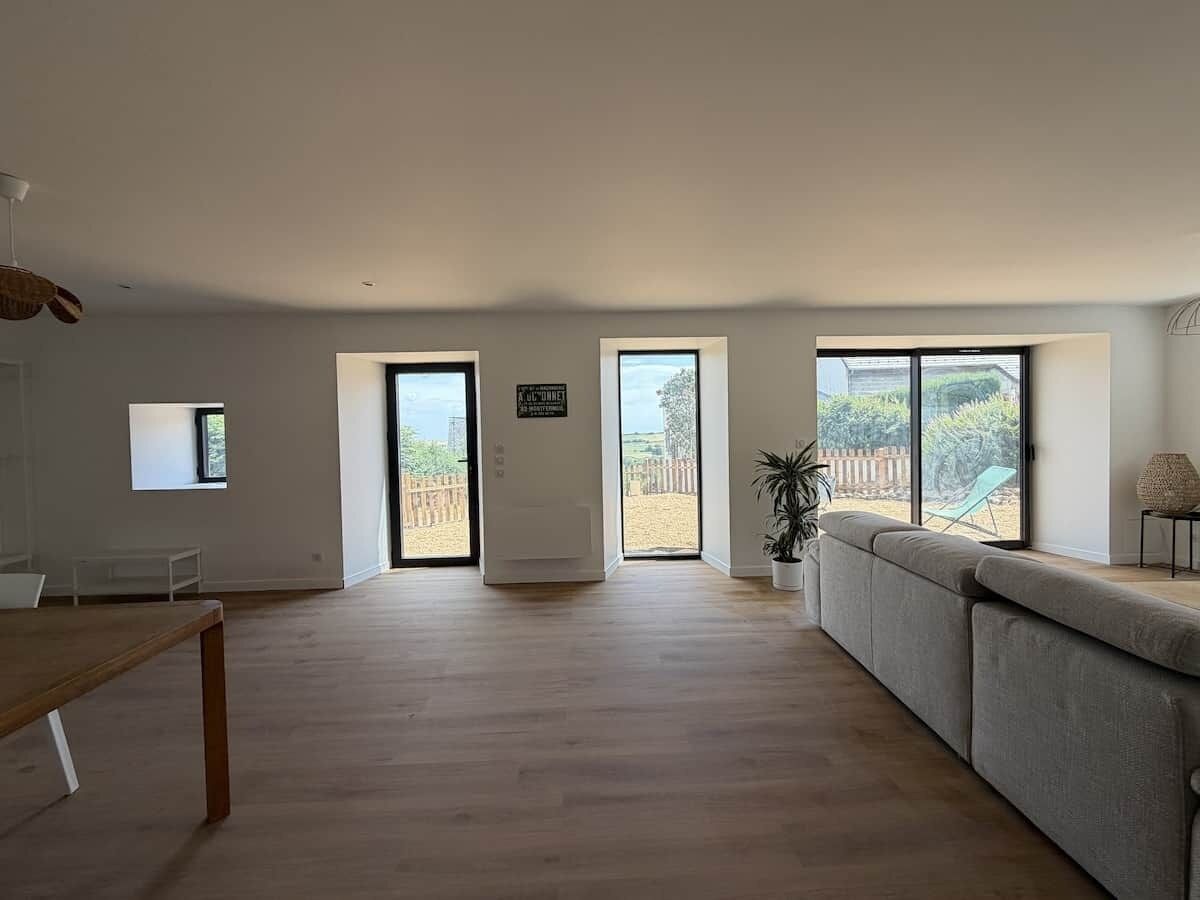 Amplia sala de estar con un sofá grande, una mesa de comedor y vistas a un patio trasero cercado a través de grandes ventanales.