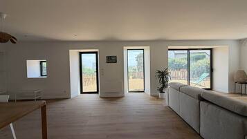 Amplia sala de estar con un sofá grande, una mesa de comedor y vistas a un patio trasero cercado a través de grandes ventanales.