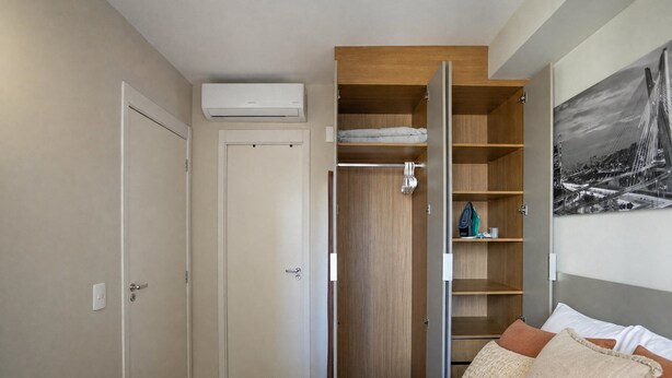 A bedroom with a bed, a wardrobe, and a wall-mounted air conditioner. - Welconx Vila Olimpia (São Paulo)