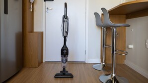 A vacuum cleaner in a room with a wooden floor, a white door, and a bar area with two stools. - Welconx Vila Olimpia (São Paulo)