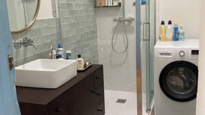 A bathroom with a sink, mirror, dark-colored cabinet, shower, and a washing machine. - Cozy house in Bordeaux in beautiful central neighborhood - near sights and tram (Bordeaux)