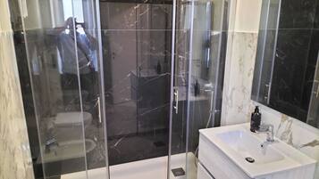 Un bagno moderno con cabina doccia in vetro, un lavandino bianco e uno specchio grande.