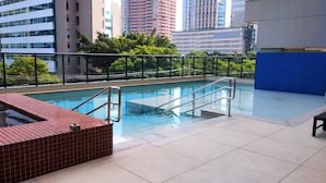 A rooftop pool with a glass barrier, a red-tiled hot tub, and a view of city buildings. - Zip Brooklin (São Paulo)