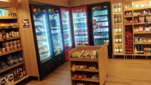 A grocery store interior with refrigerated beverage dispensers, shelves stocked with snacks, and a display of packaged goods. - Zip Brooklin (São Paulo)